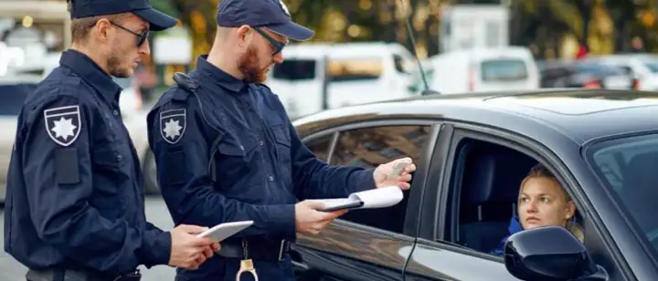 Two uniformed officers beside a car, one returning documents to the driver through the window