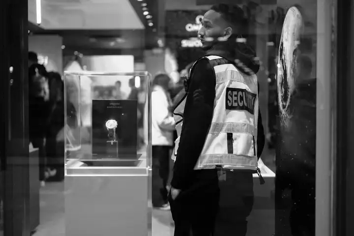 Security guard in a reflective vest standing beside a watch display case in a store
