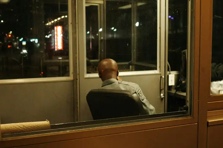 Security guard sitting alone in a lit guard booth at night