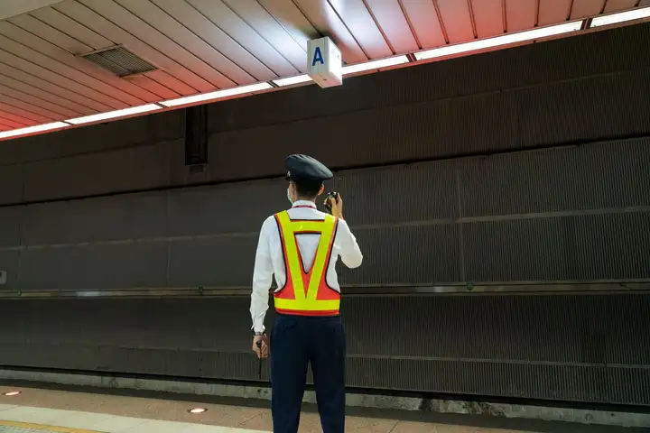 Security guard in a reflective vest talking on a radio on an empty station platform