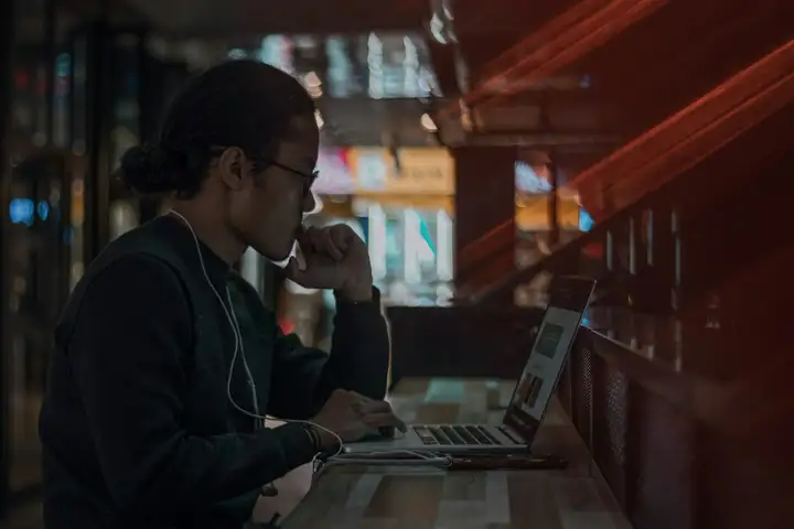 Man in glasses researching on a laptop in a dim room with red light