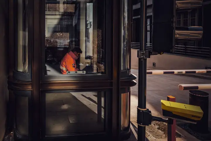 Security guard at work inside a glass guard booth beside a parking barrier
