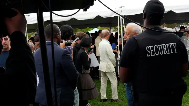 Security guard in a black SECURITY shirt watching over a crowded outdoor event under a tent