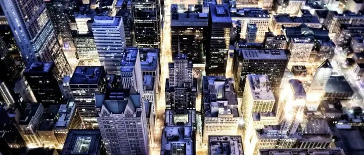 Aerial night view of a dense city with lit streets and rooftops
