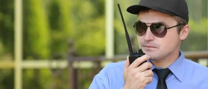 Security guard in sunglasses and a cap speaking into a two-way radio outdoors