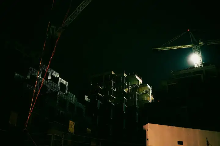 Building under construction with a lit tower crane at night