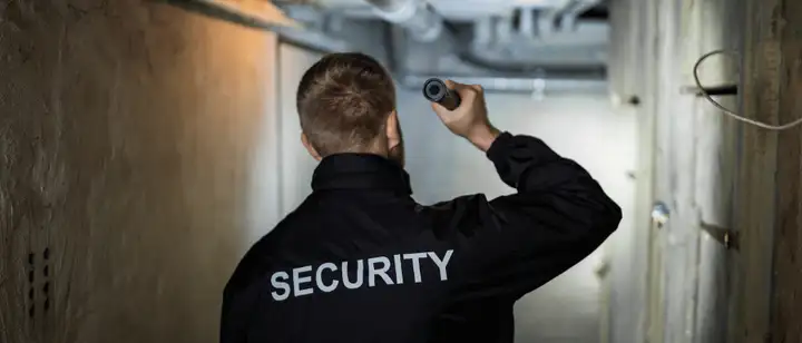 Security officer shining a flashlight in a dark basement corridor