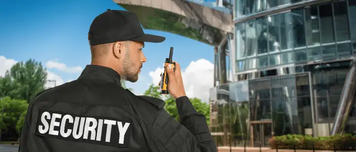 Security officer using a two-way radio outside a glass office building